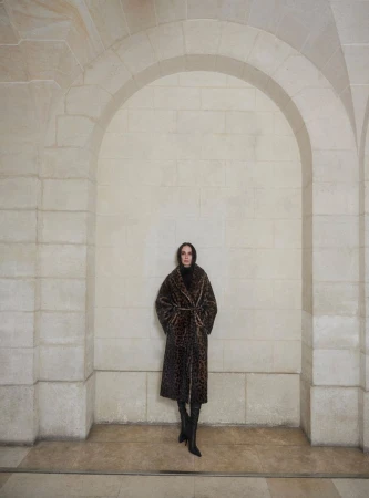 Model standing centered inside a tall stone archway wearing a leopard print coat and dark boots