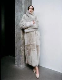Model wearing a fluffy textured cream coat standing against a concrete pillar and white wall