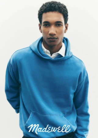 A young adult man in a blue hooded sweatshirt poses in a clean studio, showcasing the casual fashion apparel and youthful aesthetic.