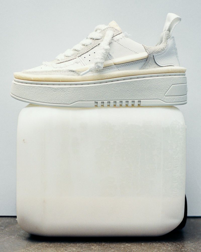 Elevated view of a white sneaker displayed on a white cube against a seamless white background, studio lighting, fashion advertising.