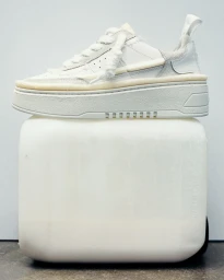 White sneaker resting on a large white block against a plain light background