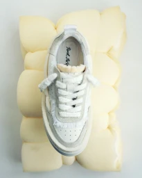 Axel Arigato sneaker resting upright on a textured yellow foam block against a white background