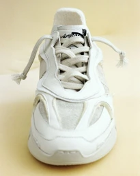 Close-up front view of a white Axel Arigato sneaker with textured panels and loose knotted laces on a plain background