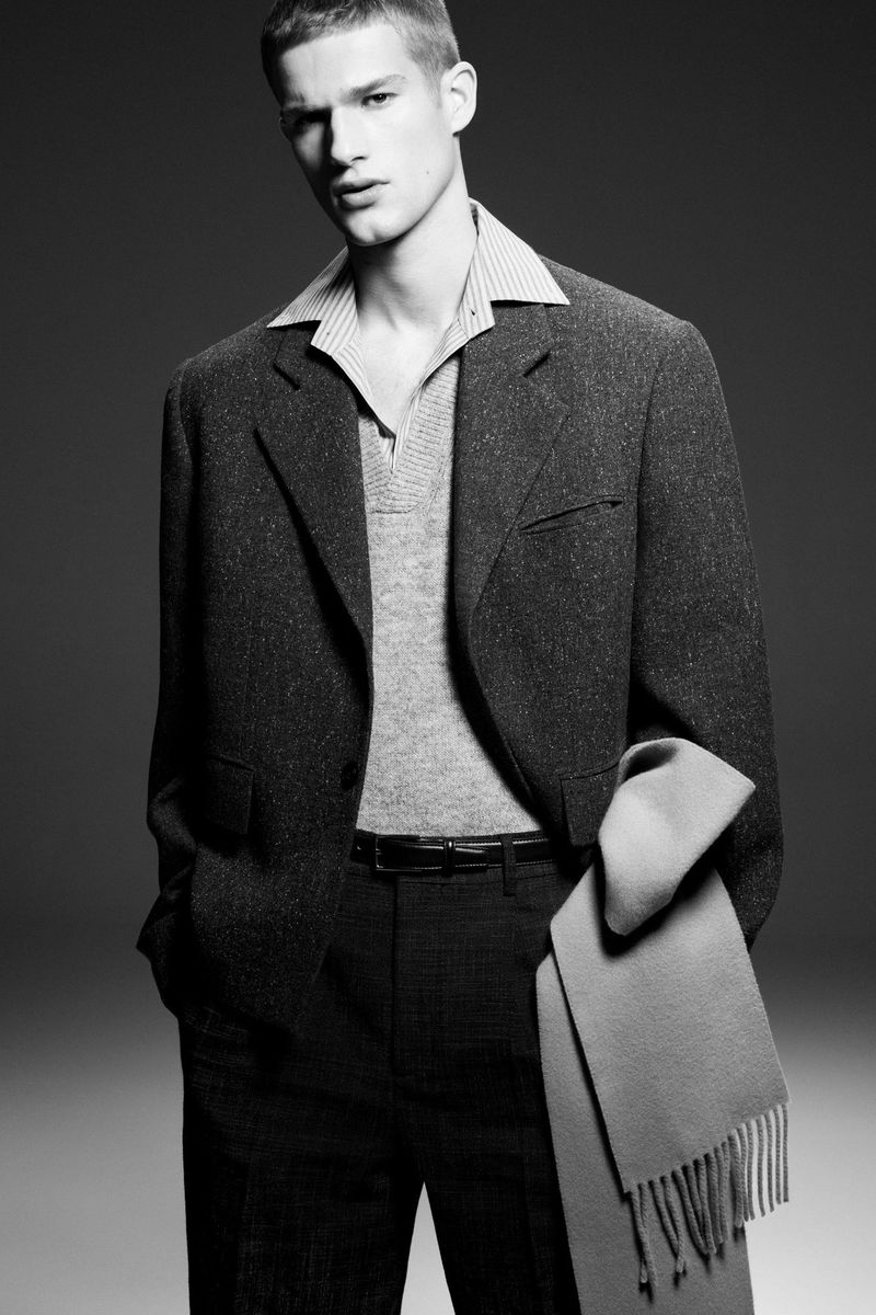 Monochrome fashion portrait of a male model wearing a dark blazer over a collared shirt against a grey seamless backdrop