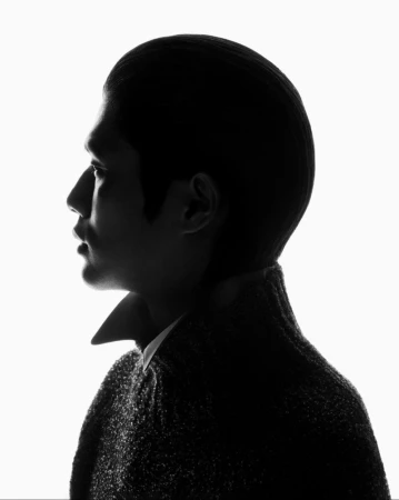 Profile silhouette of a male model wearing a high-collared textured sweater against a bright white background.