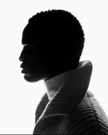 Profile silhouette of a Black model in a ribbed turtleneck and collared coat against a bright white background