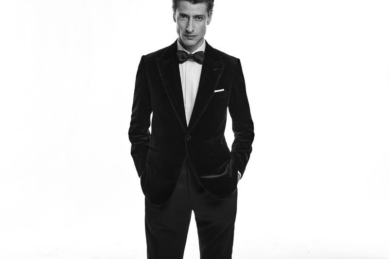 Portrait of a man wearing a black velvet tuxedo with a bow tie against a white background in a studio setting.