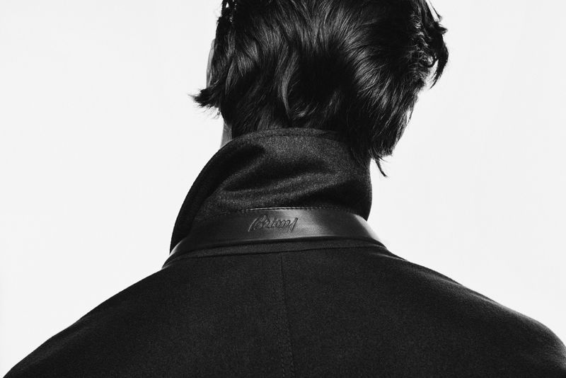 Close-up of the back of an adult male's head and shoulders wearing a dark wool coat with a leather collar, against a white background.