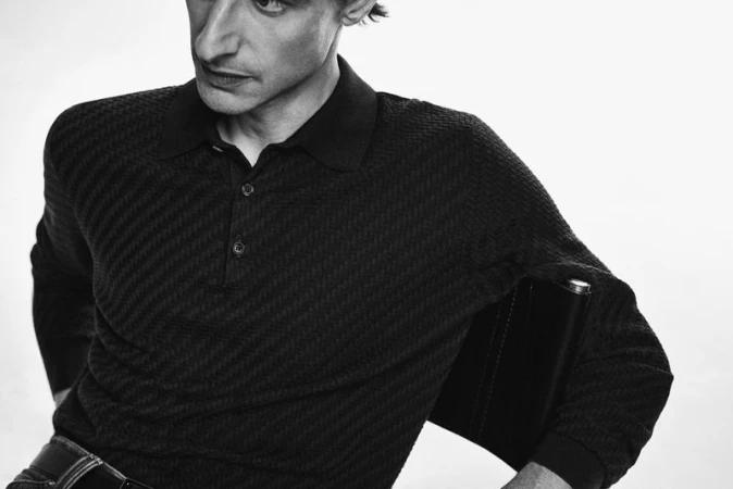 Close-up portrait of a man wearing a black textured knit polo shirt against a plain white background for Brioni FW 24.