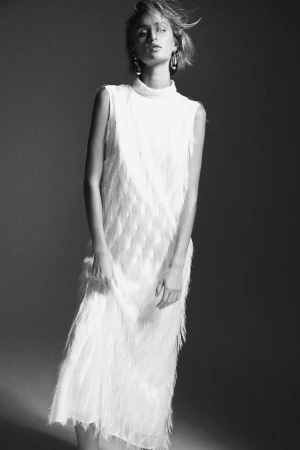 Model wearing a white fringed sleeveless dress with statement earrings in a monochrome studio lookbook image