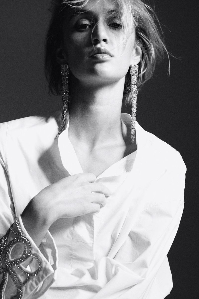 Black-and-white portrait of a fair-skinned adult female wearing long dangling earrings and an unbuttoned white shirt in a studio.