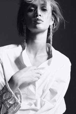 Black-and-white portrait of a fair-skinned adult female wearing long dangling earrings and an unbuttoned white shirt in a studio.