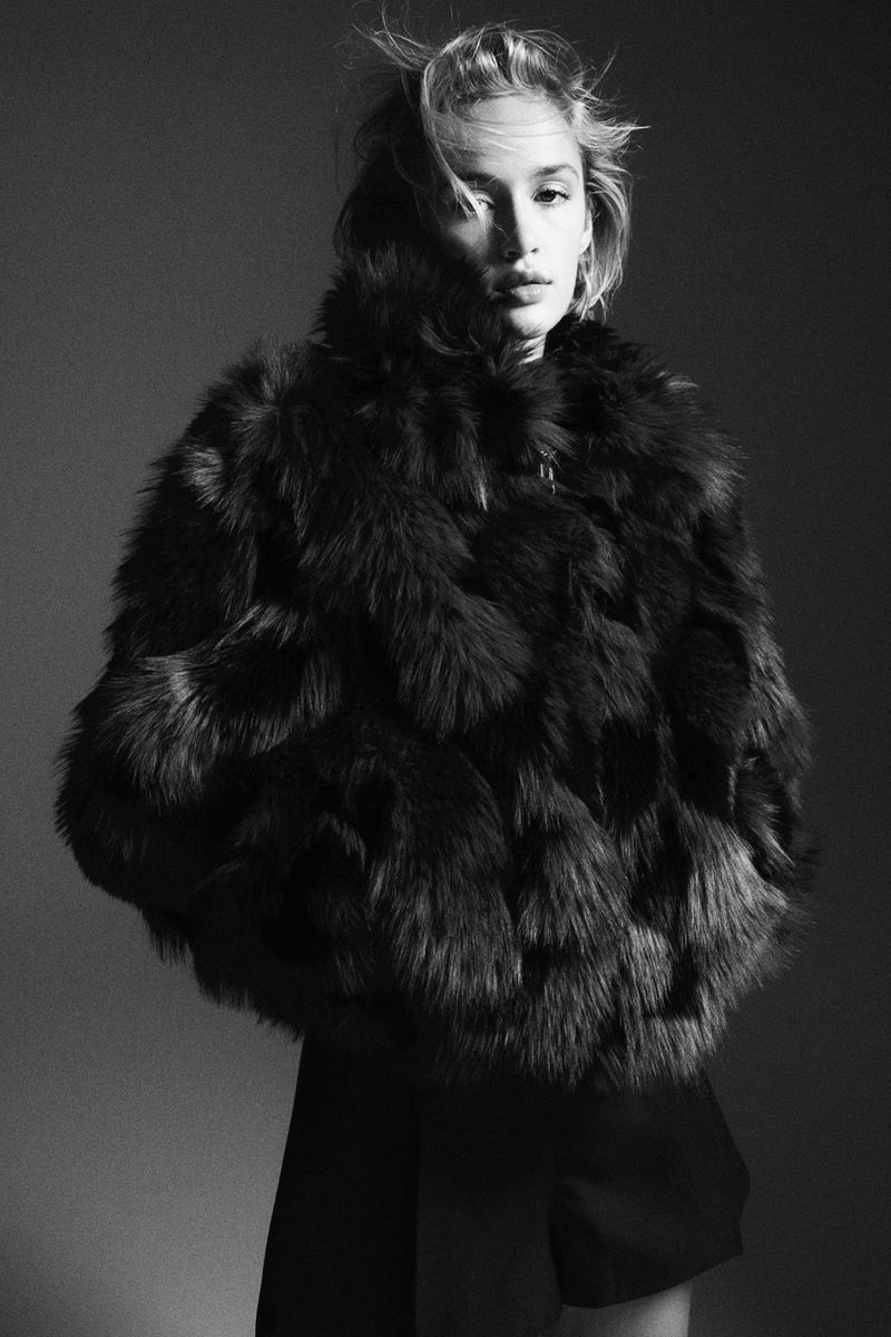 Monochrome portrait of a model wearing a textured dark fluffy jacket against a solid grey background