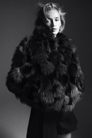 Monochrome portrait of a model wearing a textured dark fluffy jacket against a solid grey background