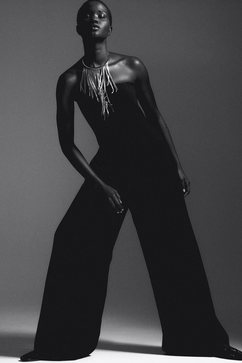 Black and white studio portrait of a Black female model in wide-leg jumpsuit with statement necklace posing against a neutral backdrop.