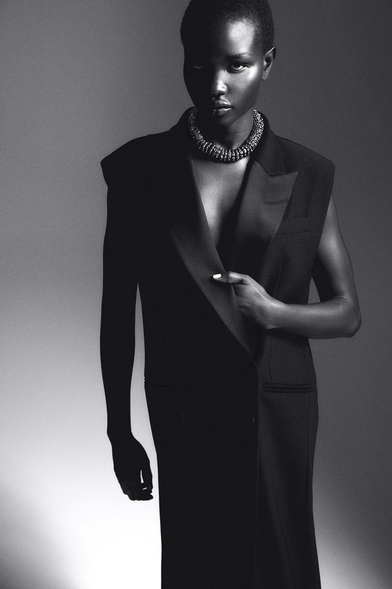 Monochrome portrait of an African-American woman wearing a black vest dress and necklace, striking a confident pose in a studio setting.