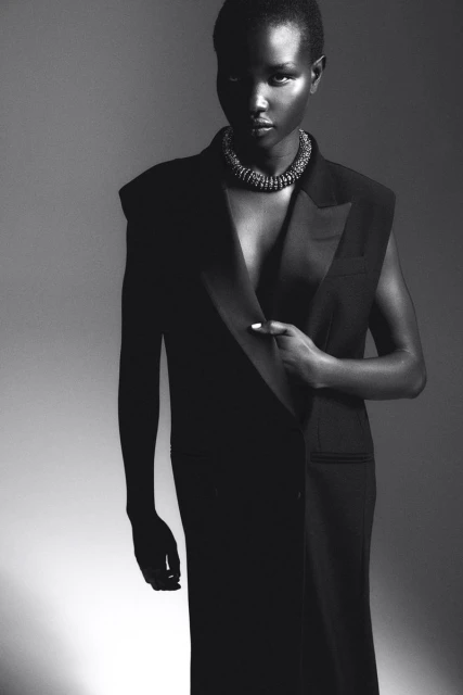 Monochrome portrait of an African-American woman wearing a black vest dress and necklace, striking a confident pose in a studio setting.