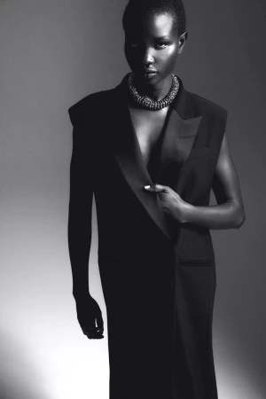 Monochrome portrait of an African-American woman wearing a black vest dress and necklace, striking a confident pose in a studio setting.