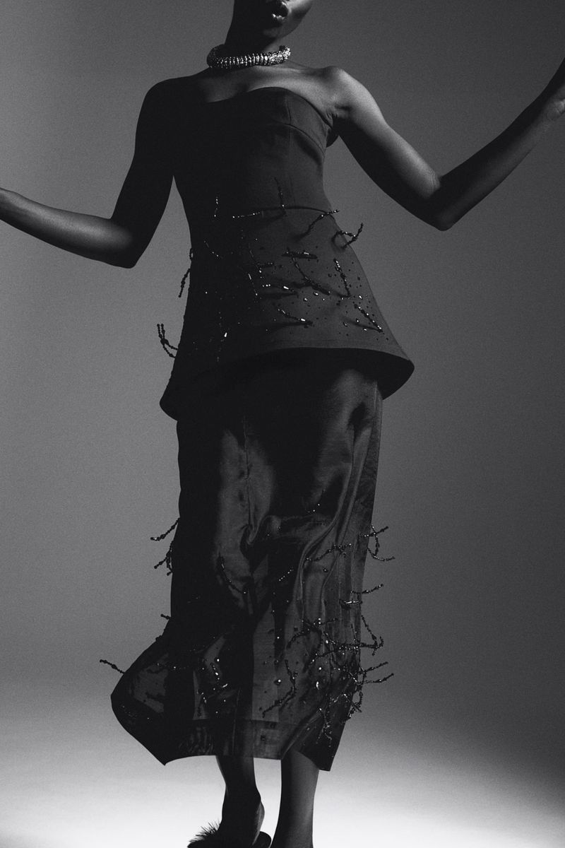Elegant studio portrait of a Black fashion model in a stylish strapless top and flowing skirt, striking a graceful pose against a grey backdrop.