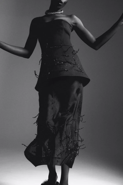 Elegant studio portrait of a Black fashion model in a stylish strapless top and flowing skirt, striking a graceful pose against a grey backdrop.