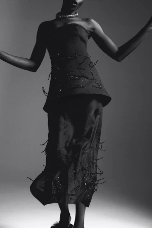 Elegant studio portrait of a Black fashion model in a stylish strapless top and flowing skirt, striking a graceful pose against a grey backdrop.