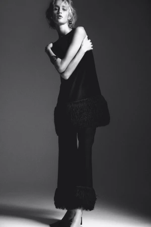 Monochrome fashion portrait of a model in a black fringe-trimmed outfit against a grey studio backdrop