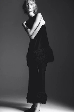 Monochrome fashion portrait of a model in a black fringe-trimmed outfit against a grey studio backdrop