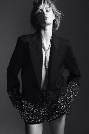 Monochrome portrait of a model wearing a tailored black blazer and embellished shorts with a sparkling necklace.