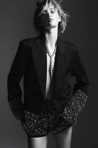 Monochrome portrait of a model wearing a tailored black blazer and embellished shorts with a sparkling necklace.