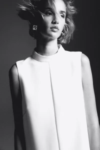 Model wearing a white sleeveless top and square earrings against a dark studio background