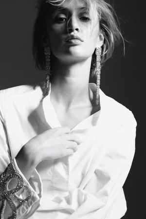 Monochrome portrait of a model wearing a white shirt and sparkling drop earrings against a dark background.