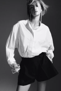 Model wearing a white button-down shirt and black shorts with sparkling crystal cuffs against a grey backdrop.