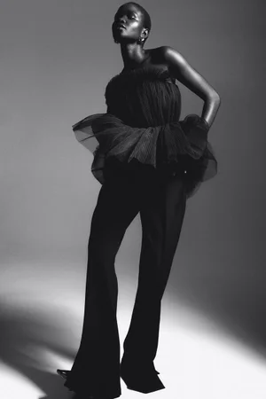 Model in black tulle top and trousers against a grey gradient studio background