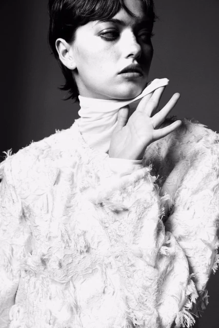 Monochrome portrait of a woman with short dark hair, wearing a white, textured top and a white scarf, against a grey background.