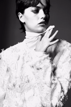 Monochrome portrait of a woman with short dark hair, wearing a white, textured top and a white scarf, against a grey background.