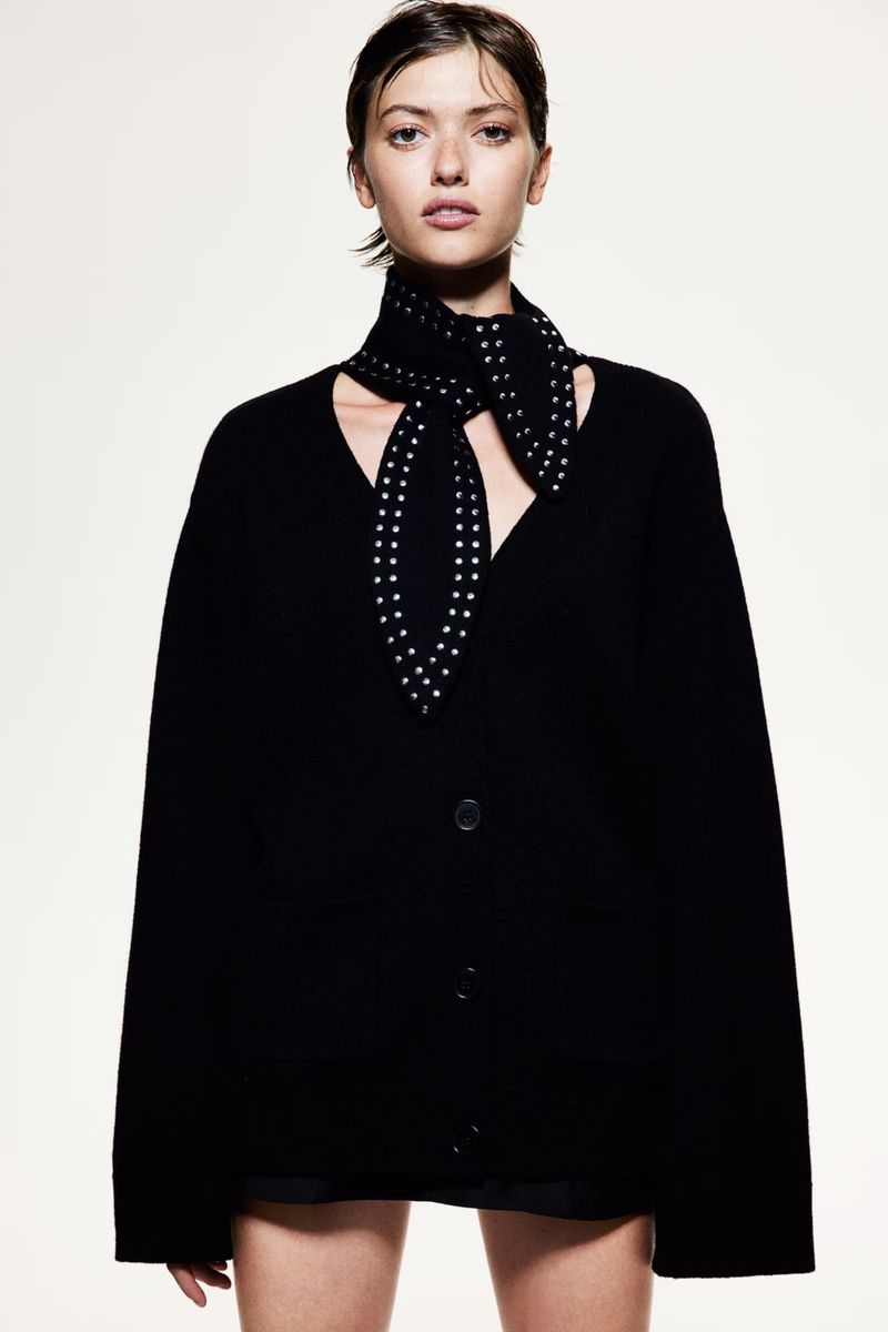 Portrait of a young adult female wearing a black cardigan sweater and patterned scarf against a bright studio backdrop.