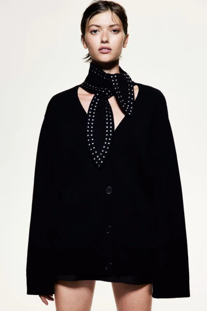 Portrait of a young adult female wearing a black cardigan sweater and patterned scarf against a bright studio backdrop.