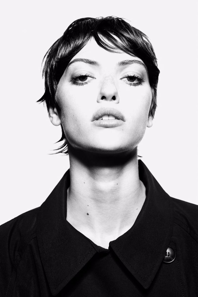 Close-up portrait of a woman with dark short hair and a black jacket against a bright white background