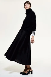 Model in black turtleneck sweater and skirt against white background for H&M