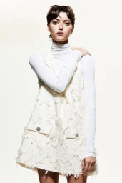 Model with short dark hair wearing a white turtleneck and textured cream dress against a bright white background