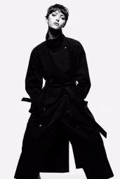 Model in a black belted trench coat against a plain white studio background