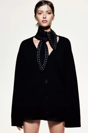Model wearing a black cardigan and studded scarf against a plain white background for H&M lookbook