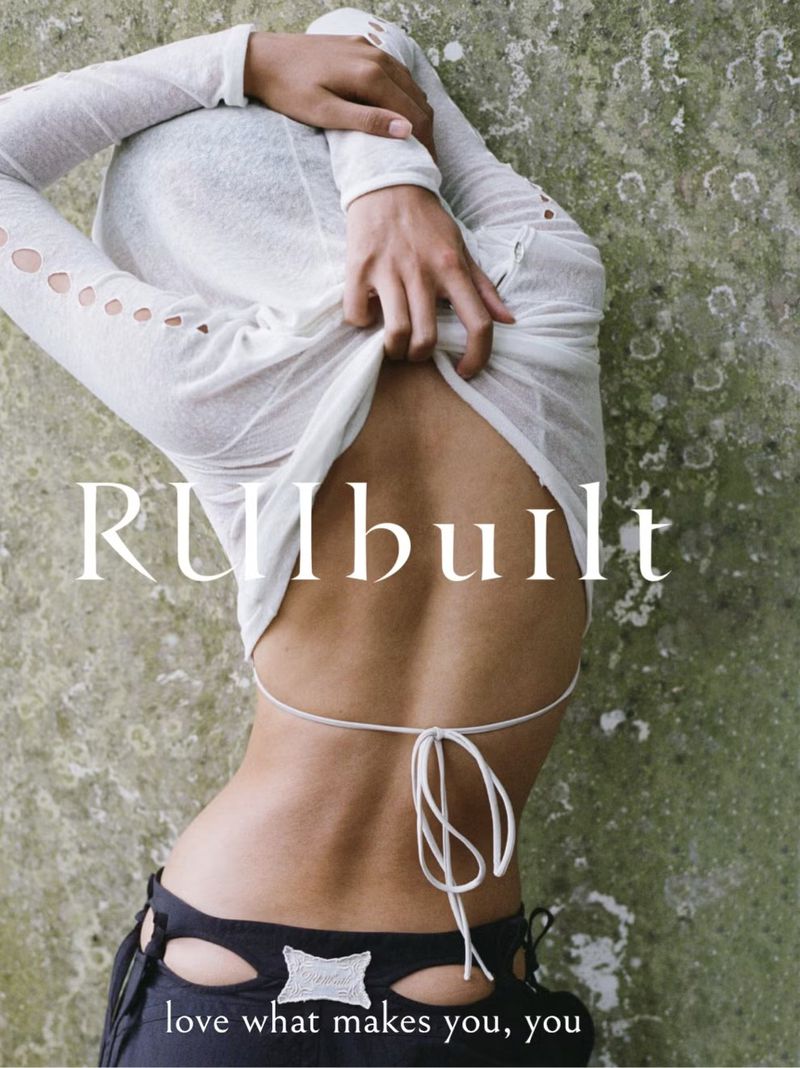 Back view of a slim woman in a white top and black pants against a textured backdrop. Body positivity message 'love what makes you, you'.