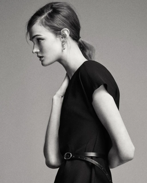 Profile view of a young woman with fair skin and a black dress in a neutral-toned studio setting. Fashion shot with a model.
