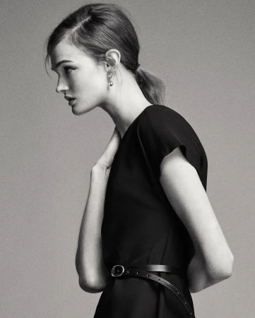 Profile view of a young woman with fair skin and a black dress in a neutral-toned studio setting. Fashion shot with a model.