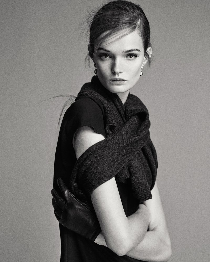 Black and white portrait of a fashionable woman wearing a black dress, leather gloves, and a dark shawl against a neutral background.
