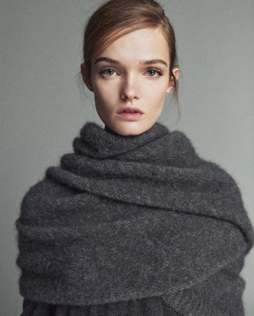 Close-up studio portrait of a fair-skinned adult female model with auburn hair wrapped in a gray wool scarf, looking at the camera.