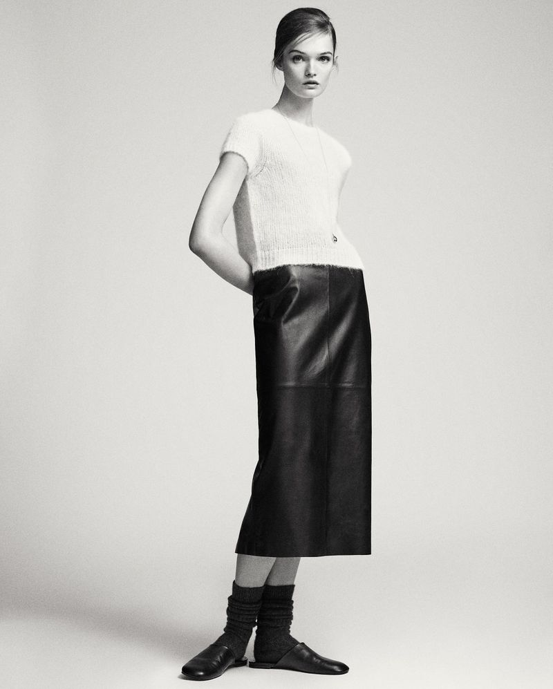 Model Lulu Tenney wearing a white textured top and black leather skirt against a seamless light grey studio background.