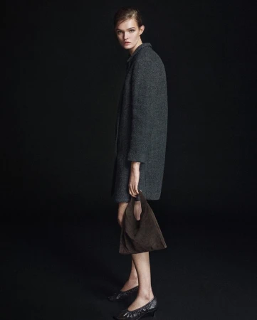 Model Lulu Tenney wearing a dark grey coat and holding a brown bag against a solid black backdrop for Massimo Dutti