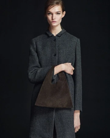Fashion shot of woman in grey coat holding a brown suede handbag against dark background. Elegant, minimalist style. Ideal for fashion blogs.